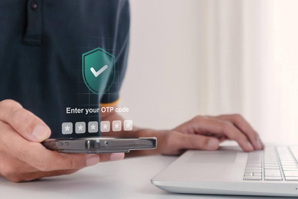 Person entering a test case for OTP verification code on a smartphone at a laptop